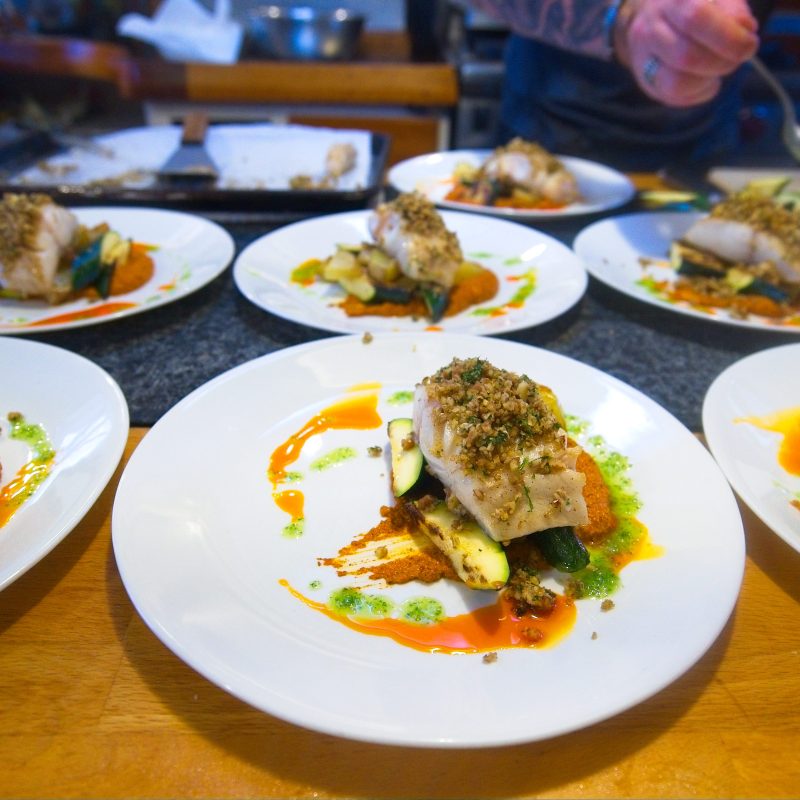 Plates of fish with vegetables and sauce being prepared on a kitchen counter.