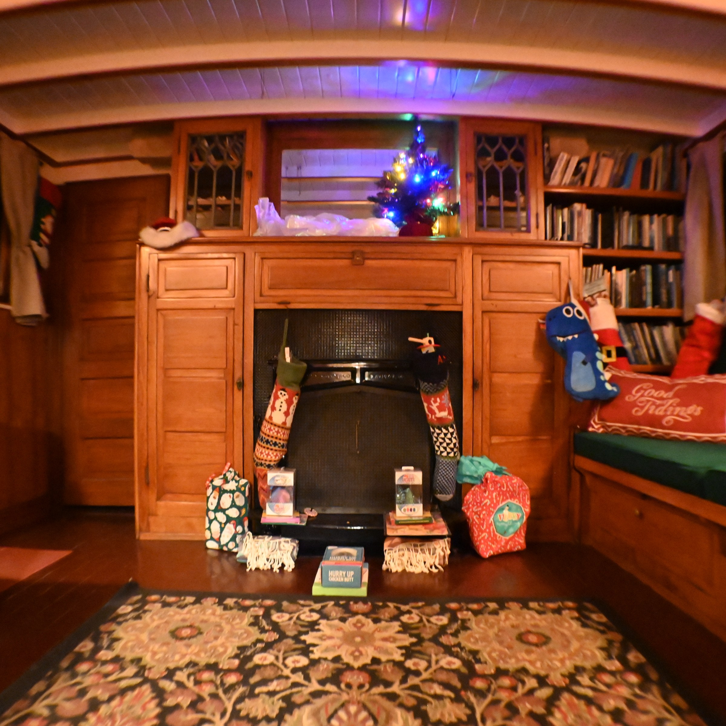 Cozy cabin with Christmas stockings, gifts, and small lit tree on a wooden fireplace.
