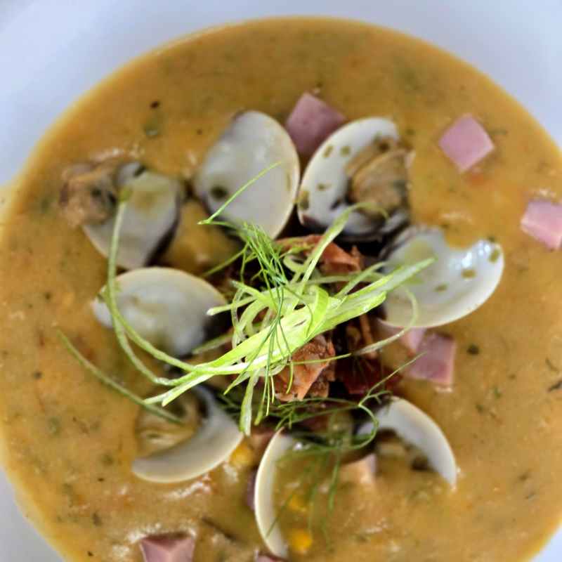 Soup with clams, cubed ham, and garnish in a white bowl.