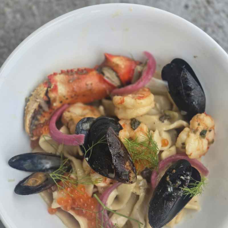 Seafood pasta with mussels, shrimp, and crab in a white bowl.
